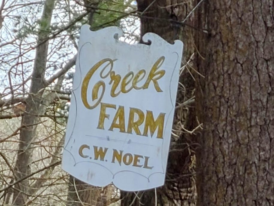 White sign with gold lettering that says Creek Farm, C.W. Noel