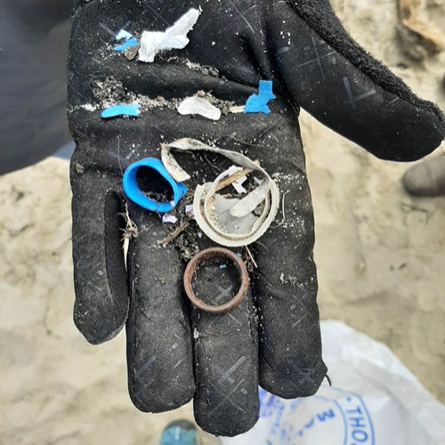 A gloved hand holding plastic litter picked up on a beach cleanup
