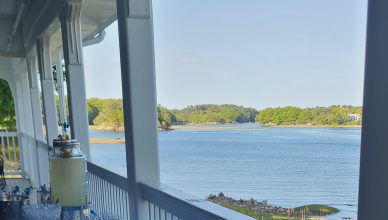 A view from the porch of a house, looking at water with trees in the background