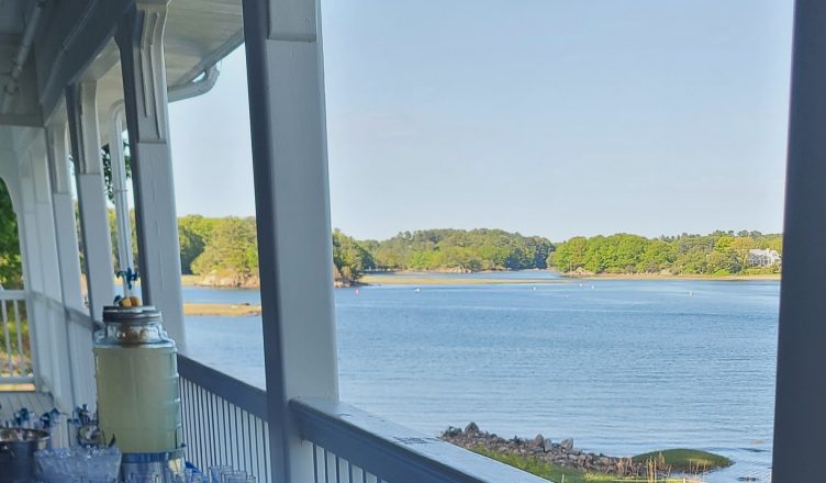 A view from the porch of a house, looking at water with trees in the background